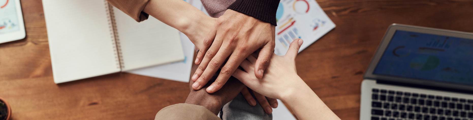 sechs Hände berühren sich über einem Tisch mit Schreibutensilien
